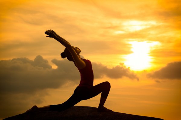 Mulher no alto de uma montanha pratica yoga com por do sol ao fundo